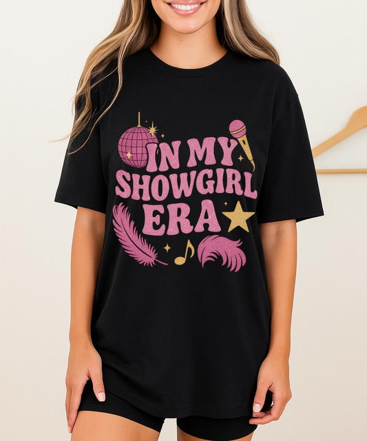 Black In My Showgirl Era shirt with pink glitter-style “In My Showgirl Era” text and disco ball, microphone, star, feather, and music note graphics.
