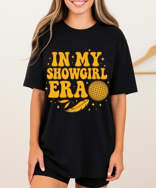 Black t-shirt with gold retro text “In My Showgirl Era” and disco ball graphic with star accents.